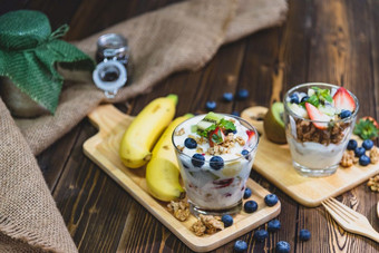 健康的希腊酸奶与格兰诺拉麦片和混合浆果木表格和许多水果食物和甜点概念