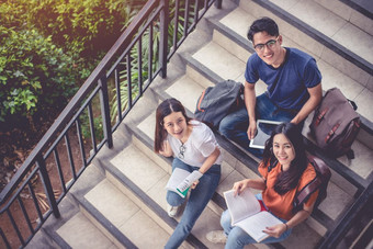 三个亚洲年轻的校园学生享受辅导和阅读书在一起楼梯友谊和教育概念校园学校和大学主题幸福和有趣的学习大学