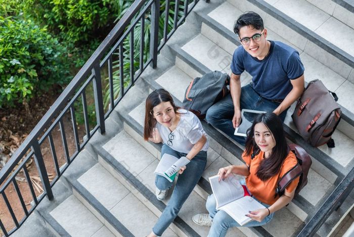 三个亚洲年轻的校园学生享受辅导和阅读书在一起图书馆楼梯友谊和教育概念校园学校和大学幸福和有趣的学习大学