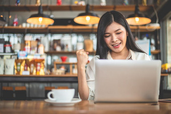 亚洲女自由职业者做快乐手势提高手当使用移动PC咖啡馆业务和成功概念咖啡商店和在户外主题自助餐厅背景