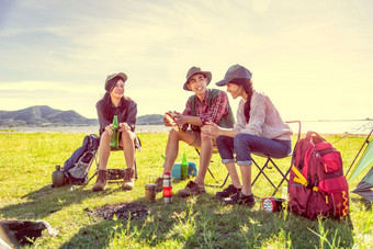 集团露营者讨论关于<strong>野餐</strong>草地场与山和湖背景人和生活方式概念徒步旅行和旅行主题三个人与背包