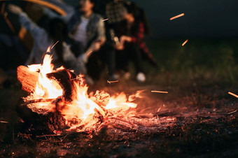 引发篝火与旅游人坐周围明亮的篝火附近野营帐篷森林夏天晚上背景集团学生户外火燃料旅行活动和长假期周末