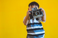 亚洲男孩持有老古董相机和摆姿势摄影黄色的孤立的背景人生活方式和技术概念
