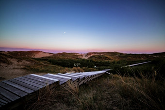 步骤沿海木木板路后日落与色彩斑斓的紫色的天空在滚动沙子沙丘和沿海植被夏天假期假期海概念