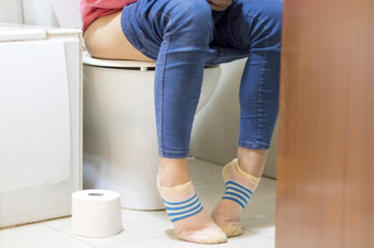 关闭照片女人与便秘腹泻坐着厕所。。。与她的裤子下来周围她的腿和纸卷的地板上