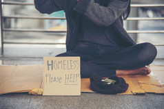 无家可归的人人贫困乞丐男人。问为钱工作和希望帮助无助的脏城市坐着与标志纸板盒子说无家可归的人请帮助董事会乞丐城市概念