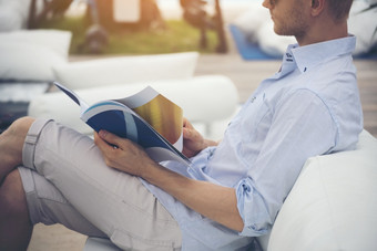 高加索人年轻的男人。阅读杂志书沙发读者持有书开放纸页面和阅读而坐着户外沙发出图书馆和阅读书生活方式为男人。