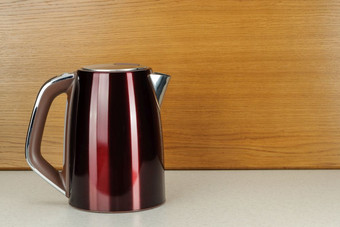 画红色的颜色不锈钢钢无线电水壶与棕色（的）塑料处理的大理石和伍迪背景与复制空间红色的不锈钢钢水壶的大理石和伍迪背景