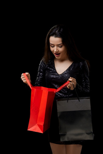 年轻的女人黑色的衣服快乐与礼物购物黑色的和红色的袋黑色的孤立的背景年轻的女人黑色的衣服快乐与礼物购物黑色的和红色的袋黑色的孤立的背景