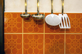 复古的厨房工具挂起古董橙色平铺的墙背景特写镜头复古的厨房工具挂起古董橙色平铺的墙背景