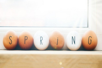 春天写鸡蛋木架子上复活节春天概念背景与阳光棕色（的）和白色鸡蛋春天写鸡蛋木架子上复活节春天概念背景与阳光
