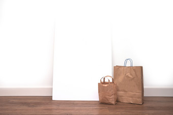 棕色（的）空白购物袋与空白海报框架对白色墙空间为文本购物概念特写镜头棕色（的）空白购物袋与空白海报框架对白色墙空间为文本购物概念