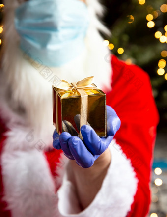 圣诞<strong>老人老人</strong>持有金礼物盒子穿保护手套和安全面具为冠状病毒新冠病毒和圣诞节概念现在圣诞<strong>老人老人</strong>持有金礼物盒子穿保护手套和安全面具为冠状病毒新冠病毒和圣诞节概念