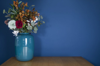 蓝色的花瓶木表格与塑料假的花花束附近蓝色的墙现代时尚的装饰生活房间与复制空间首页装饰概念空间为文本蓝色的花瓶木表格与塑料假的花花束附近蓝色的墙现代时尚的装饰生活房间与复制空间首页装饰概念