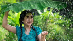 肖像年轻的亚洲女人与黑色的头发持有香蕉叶的下雨的绿色花园背景