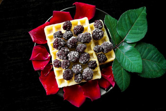 比利时华夫饼与黑莓黑色的背景与花瓣玫瑰比利时华夫饼与黑莓