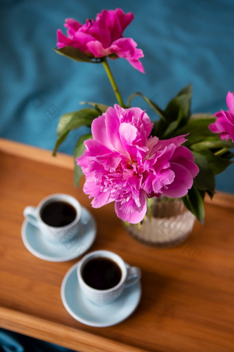 美丽的粉红色的牡丹玻璃花瓶和两个杯咖啡是站木托盘的床上特写镜头美丽的粉红色的牡丹玻璃花瓶和两个杯咖啡是站木托盘的床上特写镜头