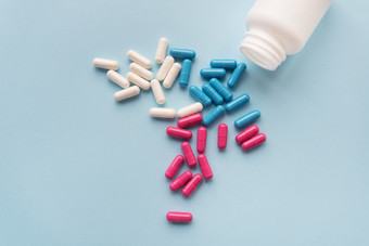 各种各样的五彩缤纷的药片蓝色的粉红色的白色飞行从开放塑料瓶孤立的光蓝色的背景各种各样的五彩缤纷的药片蓝色的粉红色的白色飞行从开放塑料瓶孤立的光蓝色的背景
