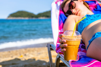 关闭女女孩女人手持有冰 沙冰咖啡的海滩而放松日光浴浴床假期阳光明媚的一天