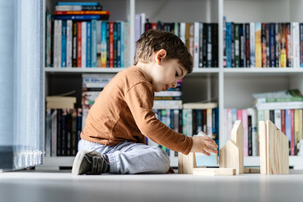 完整的长度视图小高加索人男孩小孩子首页孩子玩与木玩具砖形状房子坐着的木乙烯基层压地板上独自一人发展中创造力一边视图