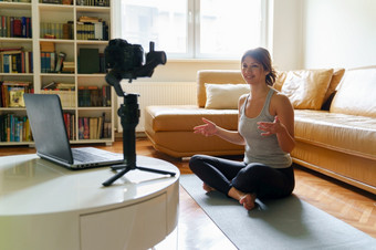 年轻的高加索人女人练习瑜伽首页美丽的教练教学在线类培训的公寓会说话的前面相机和移动PC使视频博客视频博客一天早....