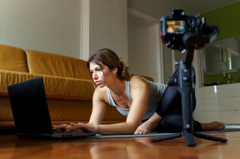 年轻的高加索人女人坐着首页美丽的教练教学在线瑜伽类培训的公寓构成体式前面相机和移动PC使视频博客视频博客一天早....