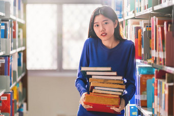亚洲年轻的学生休闲西装持有后搜索的书从书架子上图书馆大学通知书的与各种各样的书背景回来学校概念