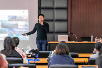 亚洲演讲者讲座与休闲西装的阶段展示通过投影仪屏幕的会议大厅研讨会会议房间观众<strong>业务</strong>教育和研讨会概念