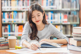 亚洲年轻的学生休闲西装阅读和做家庭作业图书馆大学通知书的与各种各样的书和静止的的木表格在的书架子上背景回来学校