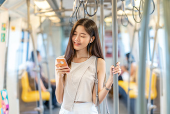 年轻的亚洲<strong>女人</strong>乘客听音乐通过聪明的移动电话地铁火车当旅行大城市日本中国人朝鲜文生活方式和每天生活通勤和运输概念