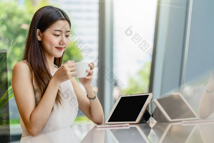 亚洲年轻的女持有杯咖啡和看平板电脑现代咖啡商店共同办公空间旁边窗口镜子日本中国人朝鲜文生活方式和每天生活企业家概念