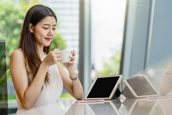亚洲年轻的女持有杯咖啡和看平板电脑现代咖啡商店共同办公空间旁边窗口镜子日本<strong>中国</strong>人朝鲜文生活方式和每天生活<strong>企业</strong>家概念