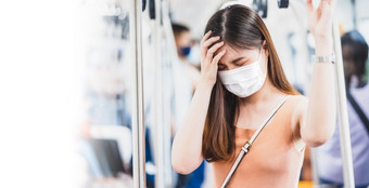 年轻的亚洲女人乘客穿外科手术面具和有头疼地铁火车当旅行大城市科维德爆发感染和流感大流行新正常的和疾病预防概念