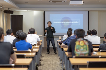 亚洲演讲者与休闲西装的阶段前面的房间与低光在的演讲屏幕的业务教育研讨会业务和教育概念