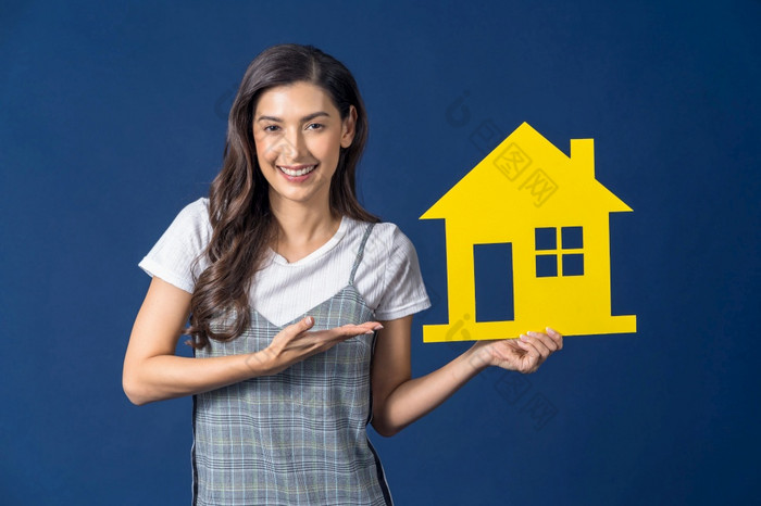 快乐年轻的微笑亚洲女人持有和展示黄色的颜色房子模型纸蓝色的颜色背景思考为投资销售和保险建筑和财产概念