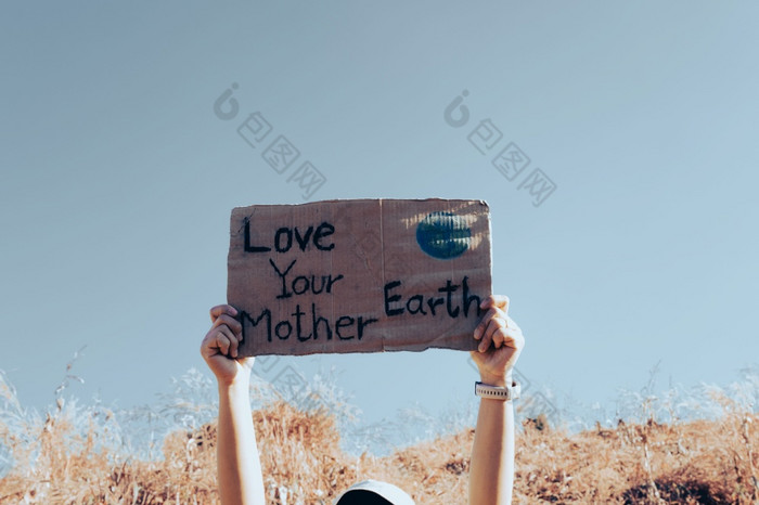 手持有持有海报与单词爱你的妈妈。地球对的背景蓝色的天空气候改变概念