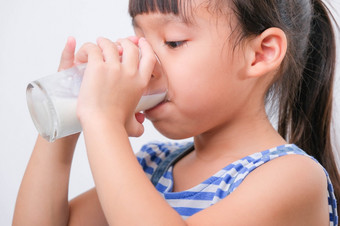 可爱的小女孩喝牛奶从玻璃孤立的白色背景小女孩享受喝牛奶之前会学校