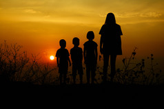 轮廓三个孩子们和妈妈站日落在那里山的背景