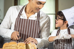 亚洲男孩穿眼镜取笑爸爸烹饪与白色面粉揉捏面包面团教孩子们实践烘焙成分面包蛋餐具厨房生活方式快乐学习生活与家庭