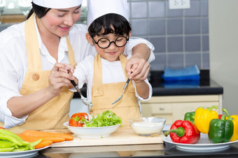 亚洲女人年轻的妈妈。与儿子男孩烹饪沙拉食物与蔬菜持有西红柿和胡萝卜贝尔辣椒板为快乐家庭烹饪食物享受生活方式厨房首页烹饪食物厨房烹饪健康的人老板准备首页高加索人年轻的准备餐新鲜的晚餐快乐有趣的女人女餐厅