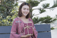 年轻的亚洲女人快乐微笑持有礼物盒子手公园