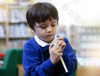 学前教育孩子享受<strong>阅读卡</strong>通的图书馆与模糊的背景书架上可爱的男孩与微笑脸而阅读最喜欢的书学校图书馆早期一年学生活动概念