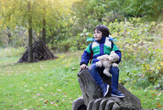 活跃的年老男孩坐着木雕像与泰迪熊孩子们穿夹克玩外森林autunmn蹒跚学步的发展概念