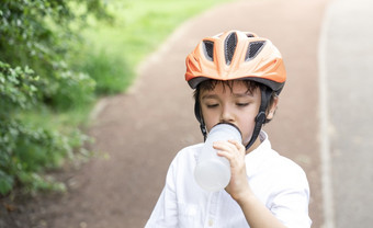 健康的孩子男孩穿自行车头盔和喝水孩子渴了男孩持有瓶水穿骑自行车头盔骑自行车的公园概念为安全童年健康哪