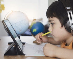 裁剪拍摄孩子使用平板电脑为他的家庭作业孩子使用数字平板电脑搜索信息互联网在首页学校教育社会距离电子学习在线教育
