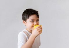 肖像年轻的孩子喝新鲜的橙色汁为早餐孤立的快乐孩子男孩喝玻璃水果汁和看相机与微笑脸健康的孩子们食物生活方式概念