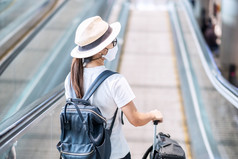 年轻的成人女穿脸面具机场终端保护冠状病毒疾病感染亚洲女人旅行者走自动扶梯飞机场新正常的和旅行下新冠病毒概念