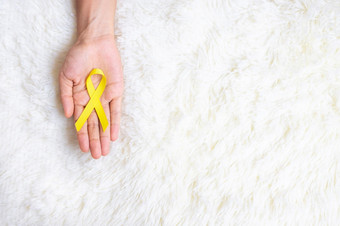 手持有黄色的丝带白色背景为支持人生活和疾病9月自杀预防一天童年癌症意识月和世界癌症一天概念