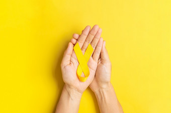 手持有黄色的丝带黄色的背景为支持人生活和疾病9月<strong>自杀预防</strong>一天童年癌症意识月和世界癌症一天概念