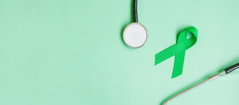 绿色丝带与听诊器绿色颜色背景为支持人生活和疾病肝胆囊甚至管癌症和器官捐赠意识月概念